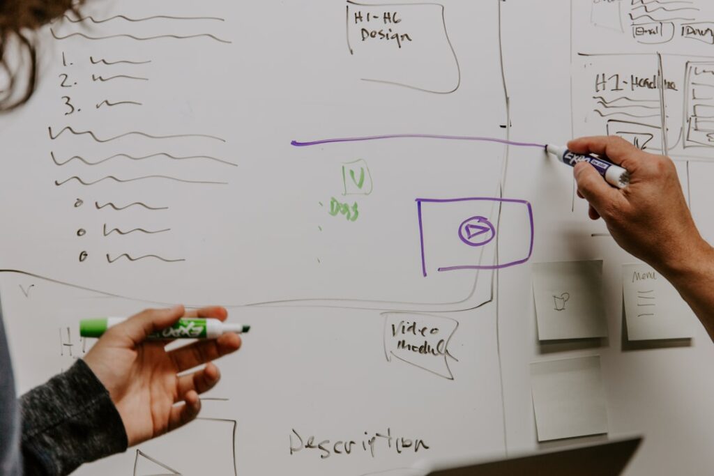 Two people sketching a landing page wireframe with CTA button and content sections on a whiteboard