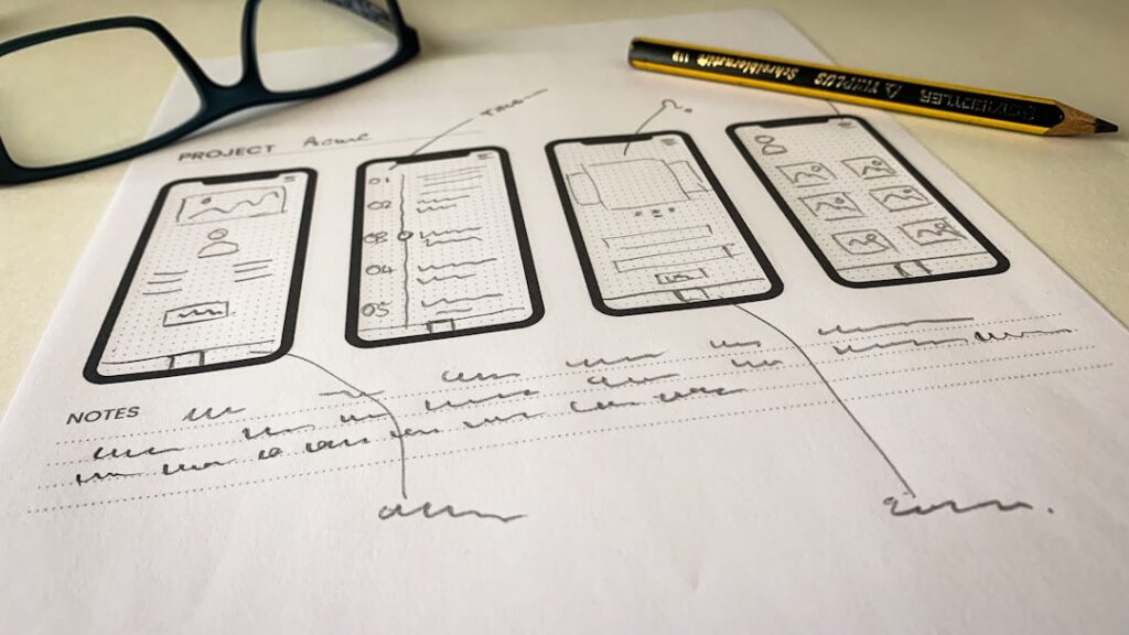 Hand-sketched mobile wireframe layouts on paper showing UX flow and page structure hierarchy