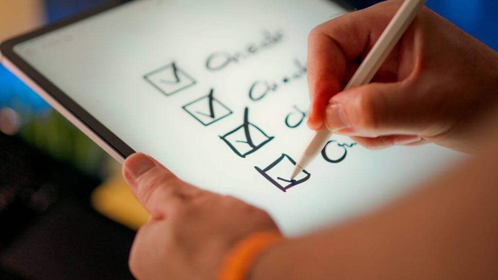 Hand using a stylus to tick checkboxes on a digital checklist on a tablet — representing a copy audit review process.